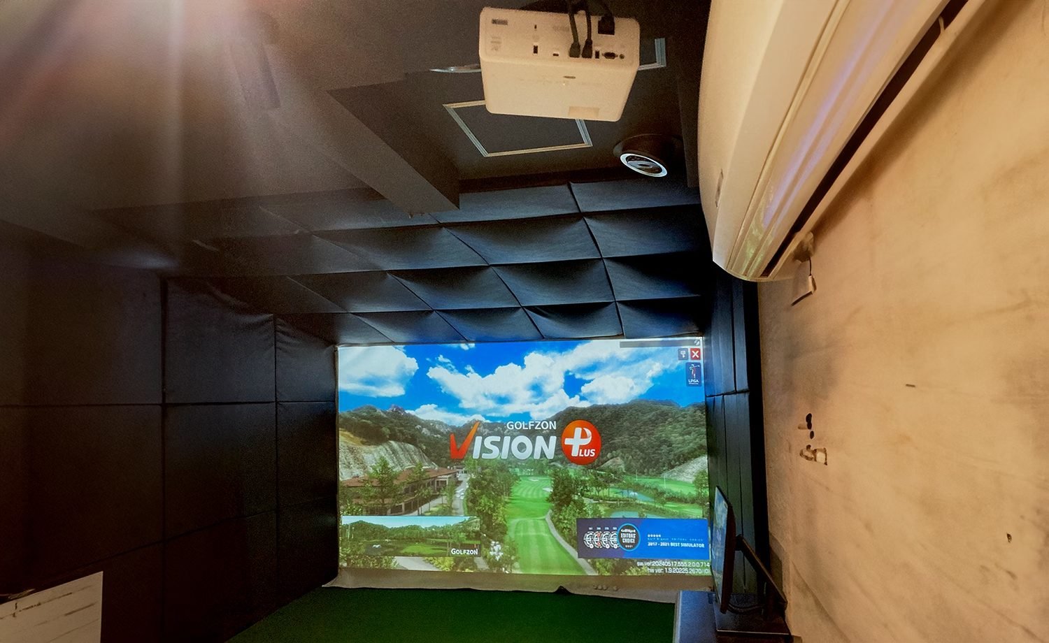 Ceiling-mounted laser projector displaying a golf simulator course on a screen